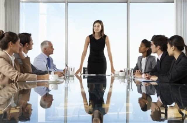 A Woman standing at the head of a boardroom table with her team looking at her from around the table.